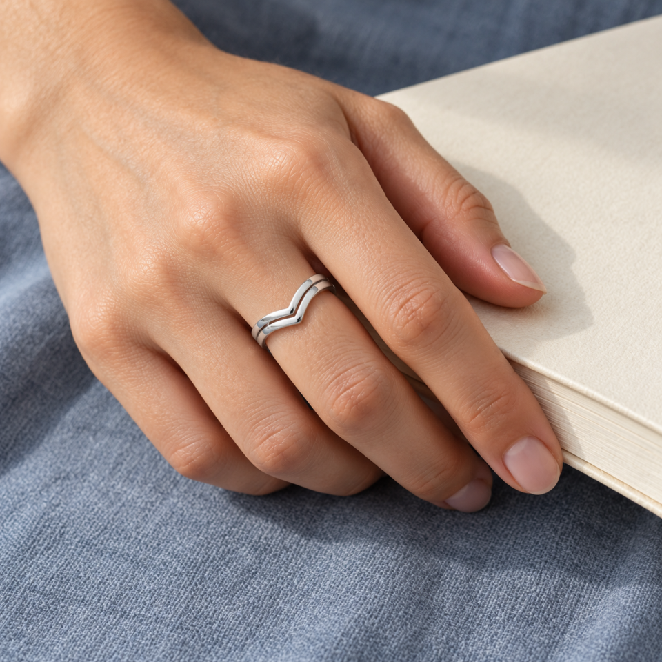 Anillo tiara doble de plata de ley 925 puesto en la mano junto a un libro