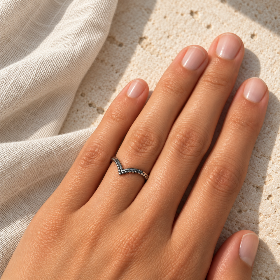Anillo fino de bolitas plateadas en forma de V puesto en una mano, sin piedras